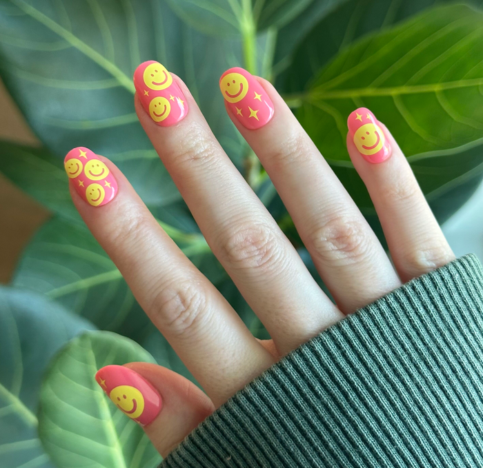 Happy All Over | Short | Round - Tab Press-On nails with pink base and yellow smiley face print for a fun mani look