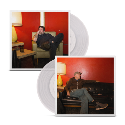 A clear vinyl peeks out of a jacket that is dual sided. On one side a man is sitting on a yellow/cream chair behind a red wall and looking to the left. On the other side, a man in a baseball cap is sitting on a black couch in the same room and looking to the right.