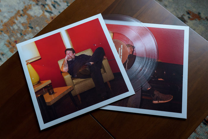 The dual sided jacket pockets and clear vinyl rest on top of a wooden table from a bird's eye view.
