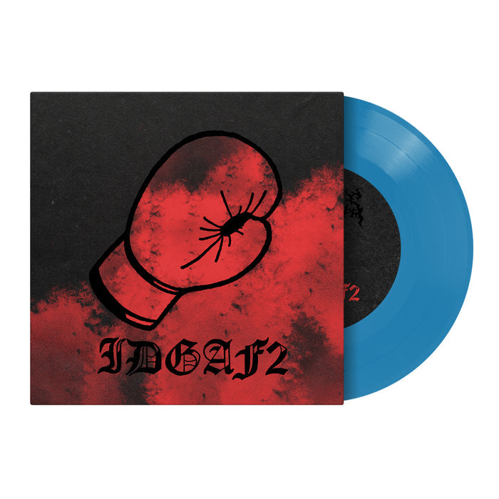A blue vinyl record by Dwellings partially slides from a black and red album cover with a red boxing glove and bold IDGAFII text, hinting at the tracklist with songs like "Just A Man.