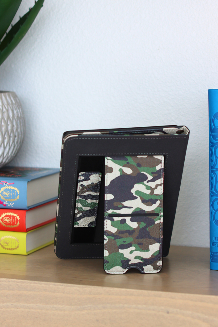 Camouflage-patterned kindle case on a wooden surface with books in the background
