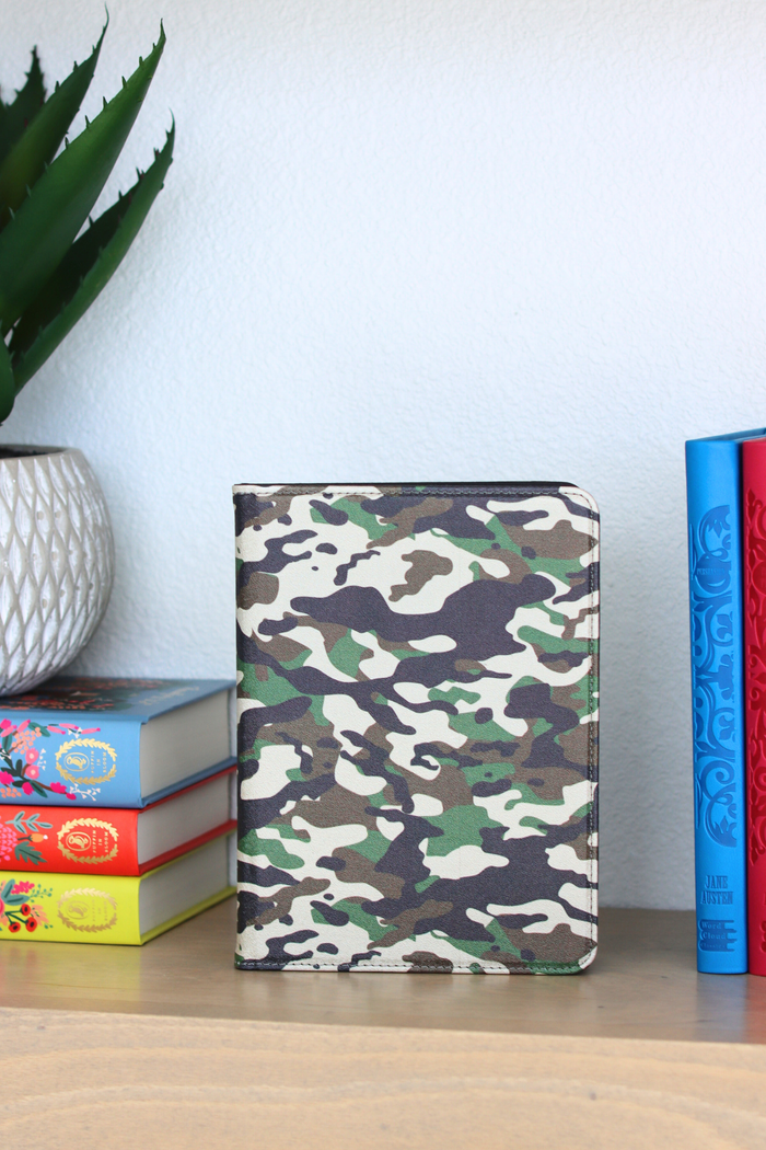 Camouflage kindle on a wooden surface with books and a plant in the background