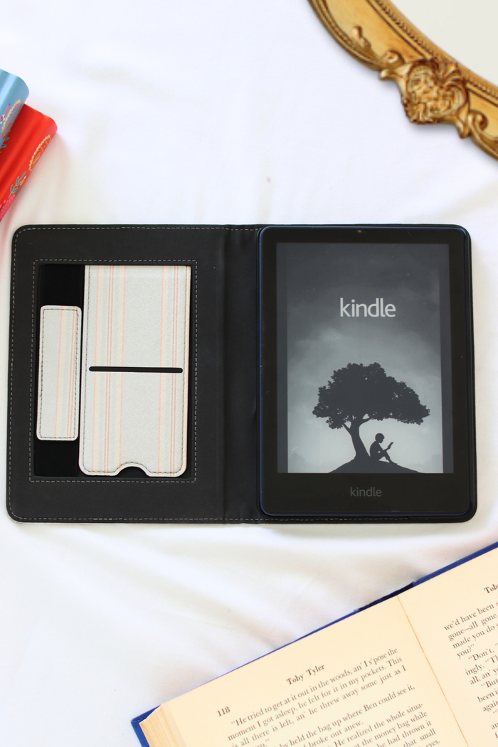 Kindle device in a black leather case on a white surface with books around