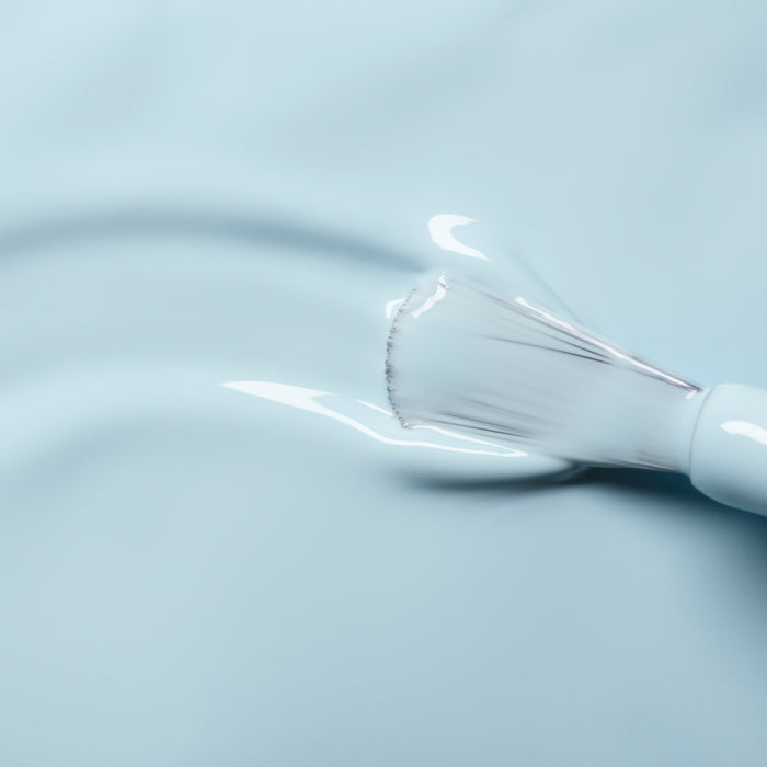 A close-up of a Manucurist Light Blue nail polish brush applying glossy, pastel blue color onto a smooth surface, creating a shiny and even coat.