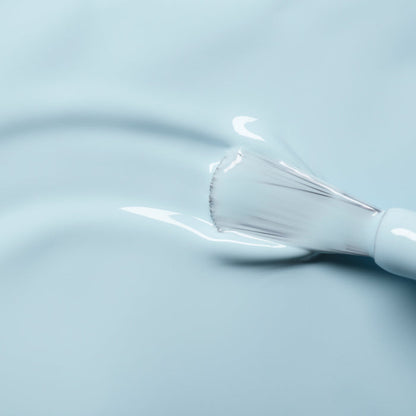 A close-up of a Manucurist Light Blue nail polish brush applying glossy, pastel blue color onto a smooth surface, creating a shiny and even coat.