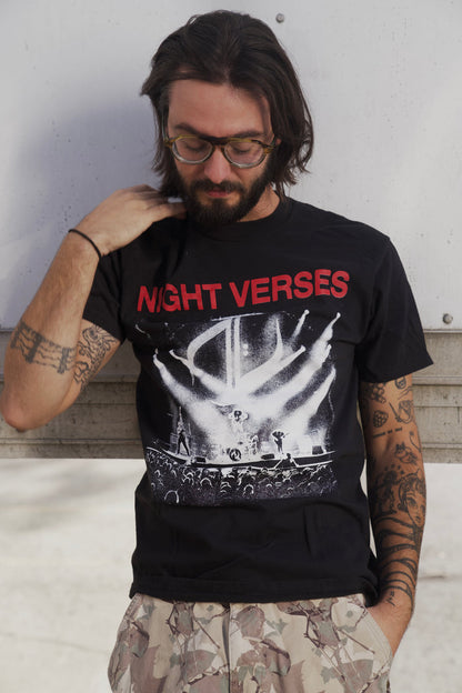 A man with long dark hair, glasses, and arm tattoos wears a soft ring-spun cotton Night Verses band t-shirt and camouflage pants, standing outdoors with his eyes down, hand touching his neck.
