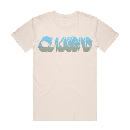 Quicksand beige Comfort Colors t-shirt with "Quicksand" in bold, rounded gradient blue letters across the chest, highlighted by a wavy sand and water effect.