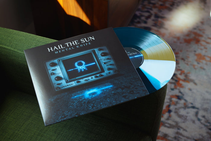 A blue and yellow Hail The Sun - Mental Knife Twister vinyl LP1, partly in its cover with a glowing blue symbol on a screen, rests on a green chair.