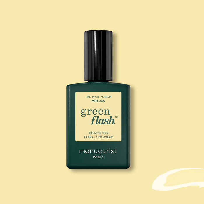 A bottle of Manucurist Mimosa Green Flash gel polish, in a dark green rectangular bottle with a black cap and pastel yellow label, is displayed on a light yellow background.