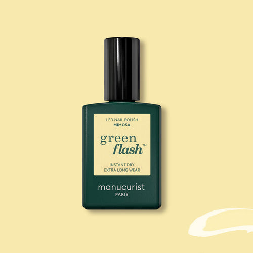 A bottle of Manucurist Mimosa Green Flash gel polish, in a dark green rectangular bottle with a black cap and pastel yellow label, is displayed on a light yellow background.