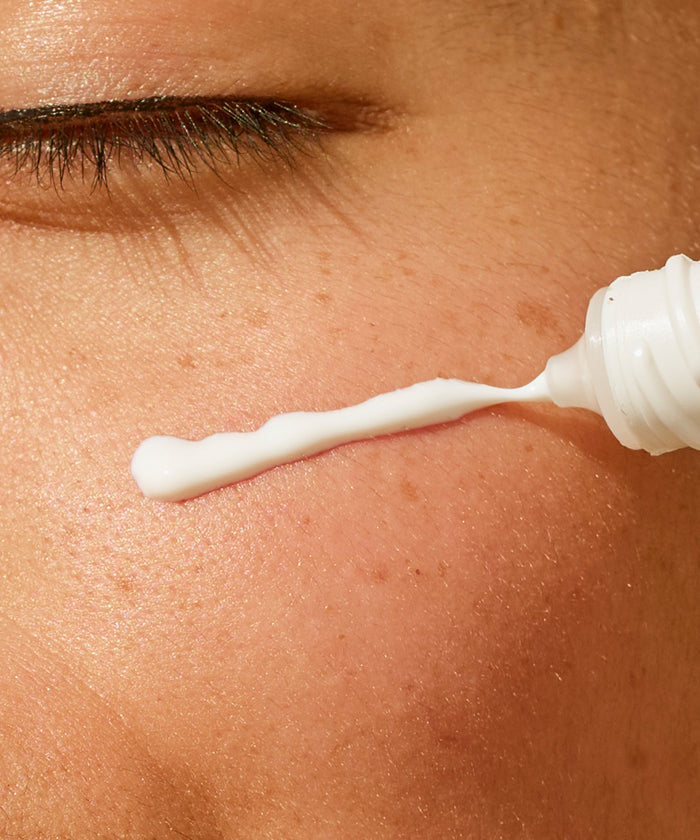 Close-up of a dropper applying white cream to skin