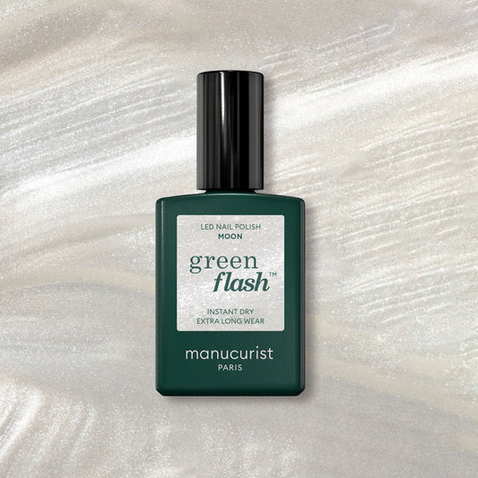 A bottle of Manucurist Moon gel polish rests on a shimmery marble background, its dark green design and white label highlighted by pearly white accents beneath.