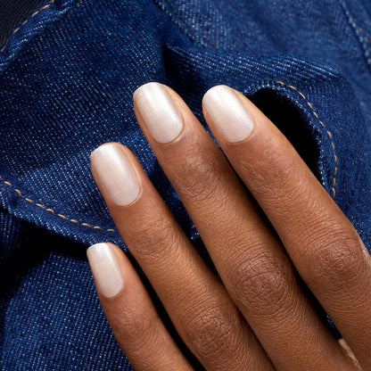 A hand with medium brown skin and neatly manicured nails painted in Manucurist Green Flash gel polish in "Moon" rests on blue denim fabric with visible stitching.