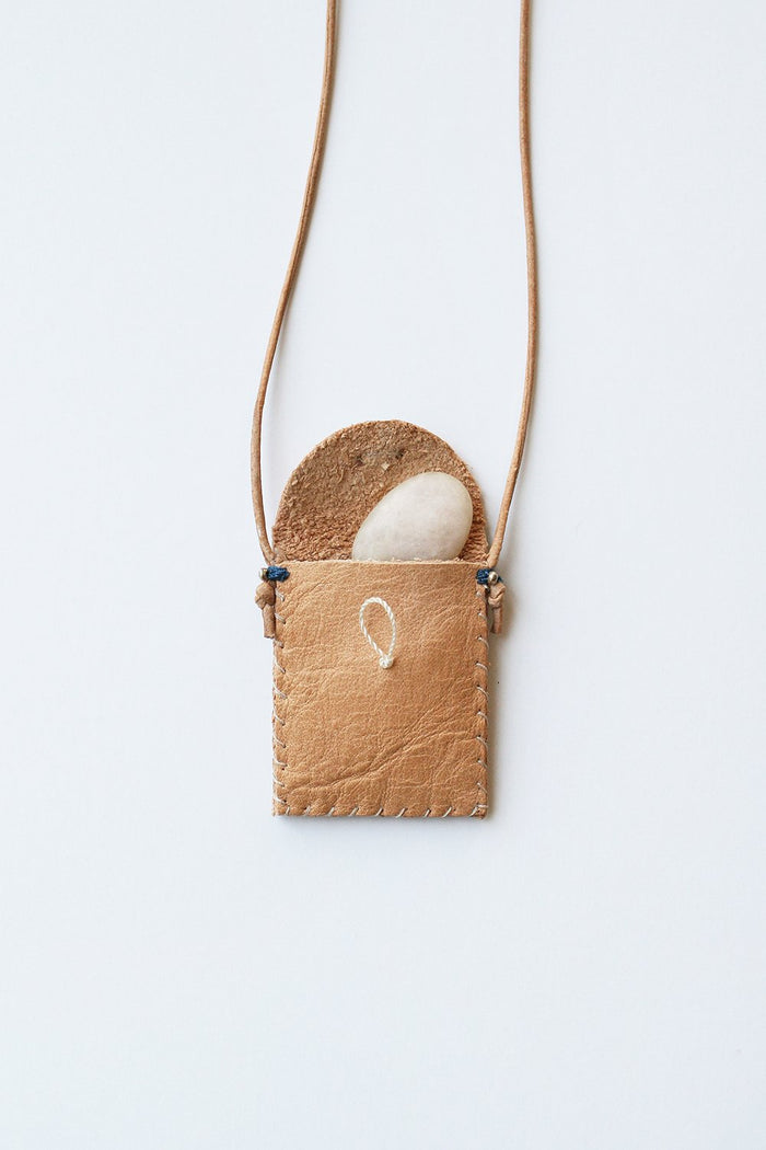 Tan leather amulet pouch with curved flap showing white stone inside