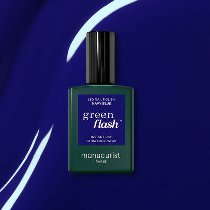 A bottle of Manucurist Navy Blue gel polish sits on a shiny deep blue surface with white curved light reflections.