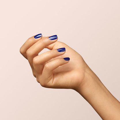 A hand with medium skin tone is held up against a plain light background, displaying neatly manicured nails painted in Manucurist’s Navy Blue gel polish.