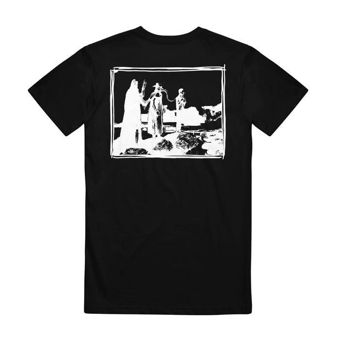 Mella black graphic tee featuring a white rectangle on the back with three abstract silhouetted figures outdoors—one holding an object—rocky ground below, and the phrase “Or So I’ve Been Told” as a subtle detail.