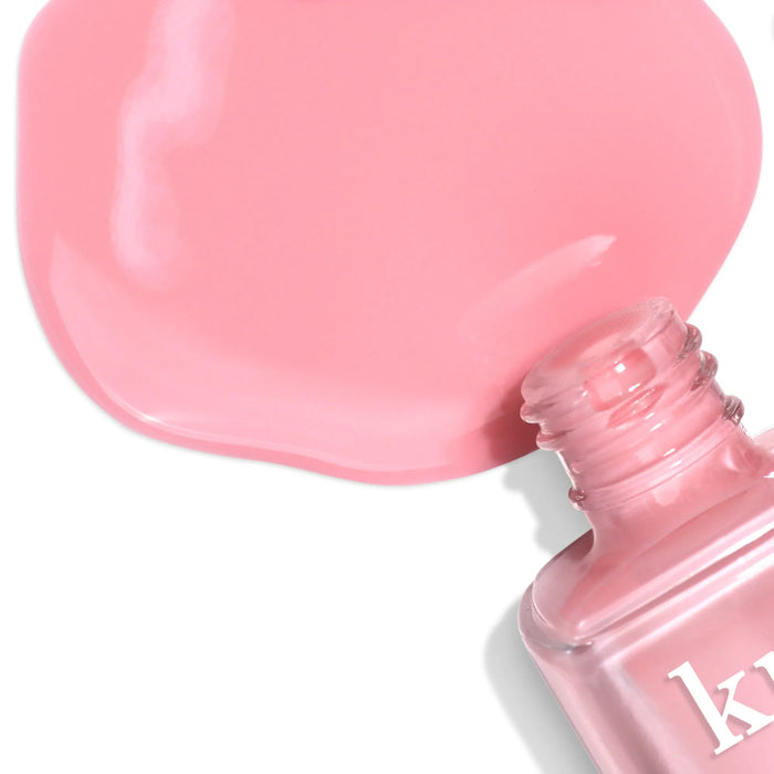 A bottle of LONDONTOWN’s Perfecting Nail Veil #7 spills pink polish on a white surface, evoking the smooth glide of a nourishing tinted lip balm for flawless care.
