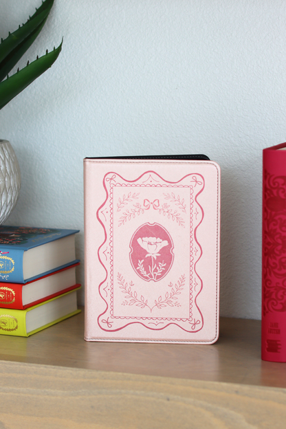 Pink kindle with decorative cover on a wooden surface with books in the background