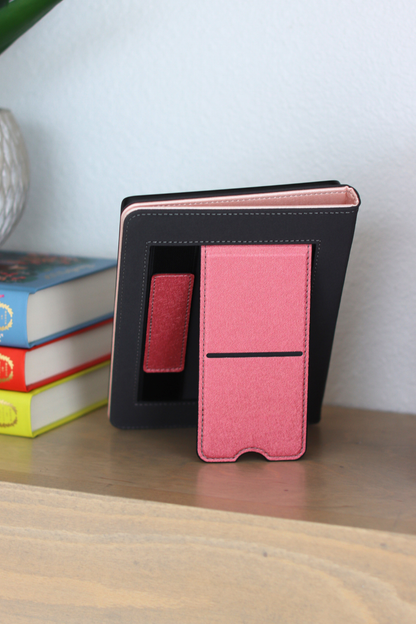 Black and pink kindle on a wooden surface with books in the background