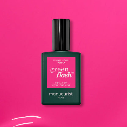 A green bottle of Manucurist’s Pétula pink gel polish rests on a vibrant pink background. This summer shade delivers instant dry, extra long wear, and subtle blue undertones for standout nails.