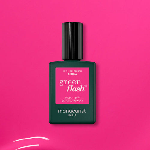A green bottle of Manucurist’s Pétula pink gel polish rests on a vibrant pink background. This summer shade delivers instant dry, extra long wear, and subtle blue undertones for standout nails.