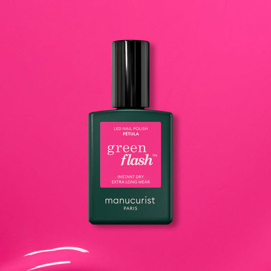 A green bottle of Manucurist’s Pétula pink gel polish rests on a vibrant pink background. This summer shade delivers instant dry, extra long wear, and subtle blue undertones for standout nails.