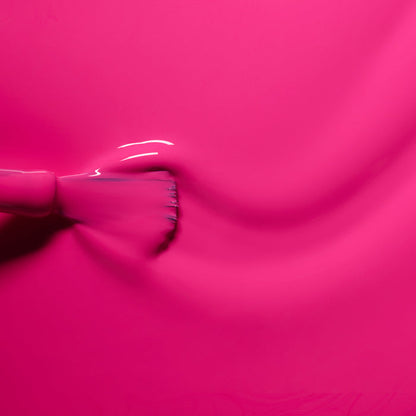 A close-up of a brush gliding through Manucurist’s Pétula, a smooth, bright pink Green Flash gel polish with blue undertones—creating glossy ripples and perfect summer nail inspiration.