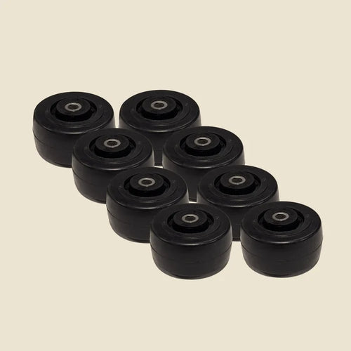 Set of eight black Pilates reformer guide wheels with steel bearings on beige background.
