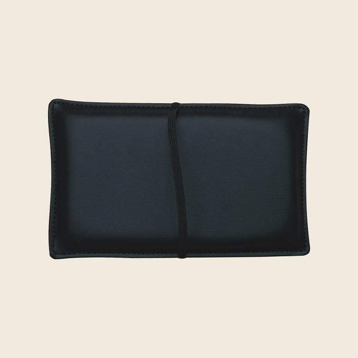 Black upholstered Pilates shoulder block pillow with strap on a neutral background.