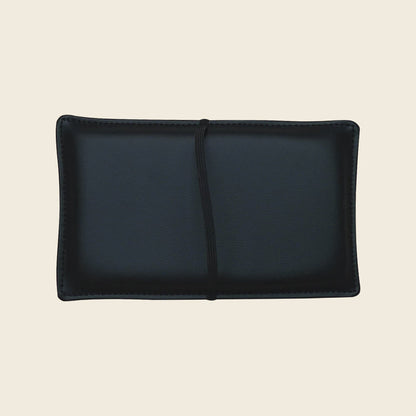 Black upholstered Pilates shoulder block pillow with strap on a neutral background.