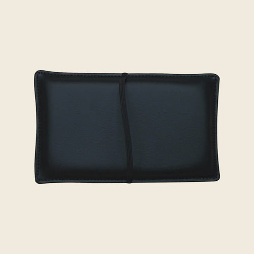 Black upholstered Pilates shoulder block pillow with strap on a neutral background.