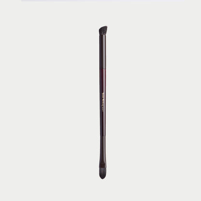 A single makeup brush with a dark metallic handle and black bristles, shown vertically against a light gray background. The handle features a metallic rose gold accent band with gold lettering that reads 'm.