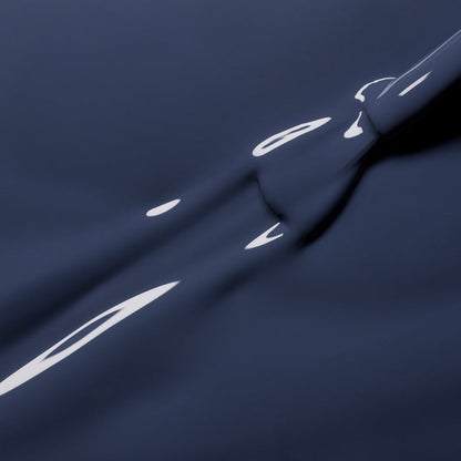 A close-up of Poppy Seed by Manucurist shows dark blue liquid with a smooth, glossy surface and reflective highlights, forming abstract shapes reminiscent of bluish grey nail polish.