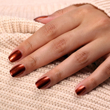 Close-up of a hand with LONDONTOWN's Posh Forever metallic bronze nail polish resting on a knitted beige fabric, evoking the warm tones of cinnamon.