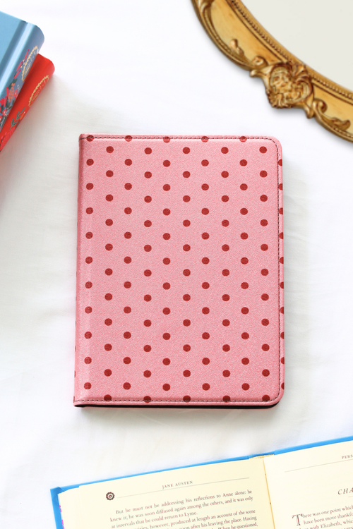 Pink polka dot kindle on a white surface with books and decorative items.