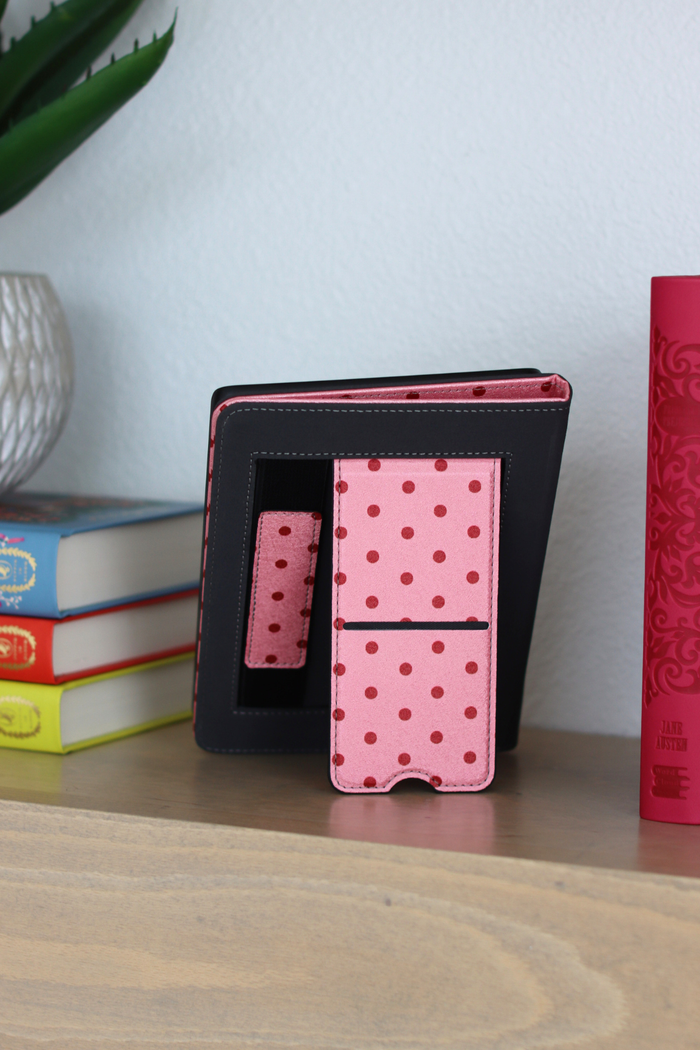Pink polka dot case on a wooden surface with books and a plant in the background