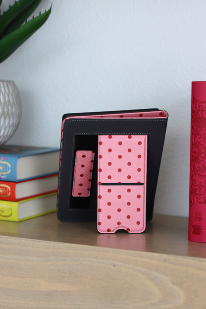 Pink polka dot case on a wooden surface with books and a plant in the background