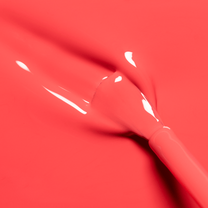 A close-up of a makeup brush spreading Manucurist’s Pulp, a bright, glossy coral pink gel polish, over a smooth surface—evoking fresh grapefruit nectar.