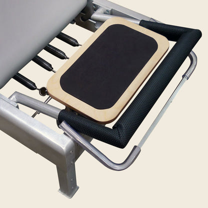 Wooden reformer standing platform with black non-slip pad mounted on a Pilates reformer frame.