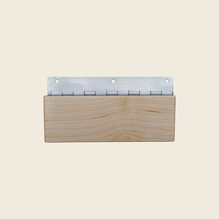Wooden Gratz reformer head rest block with metal piano hinge on a beige background.