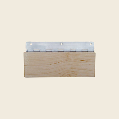 Wooden Gratz reformer head rest block with metal piano hinge on a beige background.