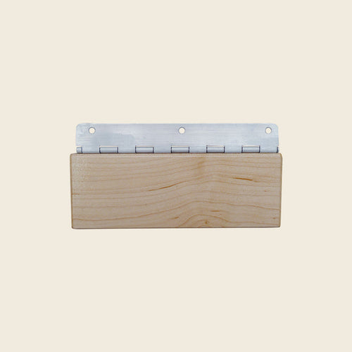 Wooden Gratz reformer head rest block with metal piano hinge on a beige background.