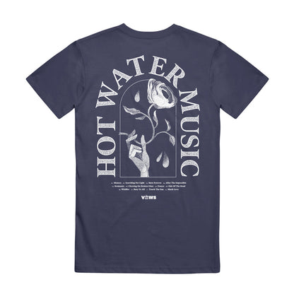 Hot Water Music navy Comfort Colors tee with bold white “HOT WATER MUSIC” text circling a white rose graphic. Tour dates/locations are in small text below, finished with the VLVVS logo.