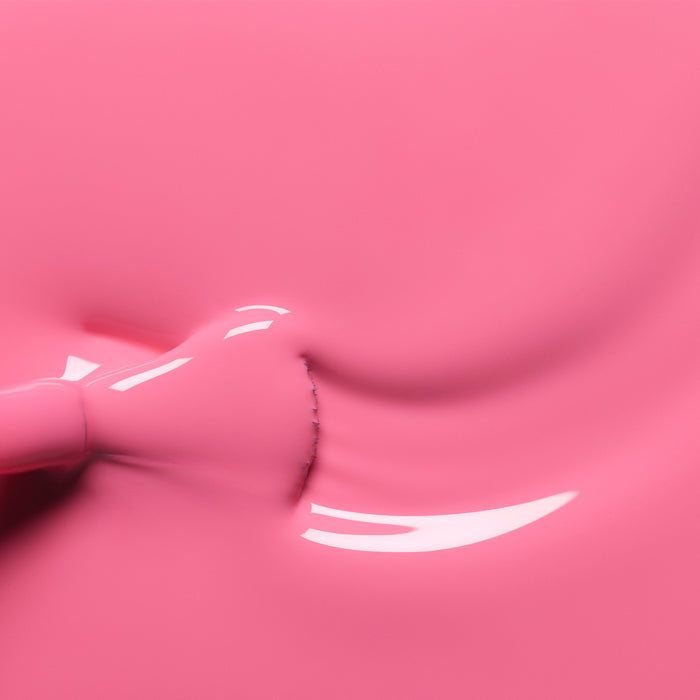 Close-up of Manucurist’s Rose pink nail polish spreading smoothly, showing glossy reflections on the liquid surface as a brush is partially visible on the left.