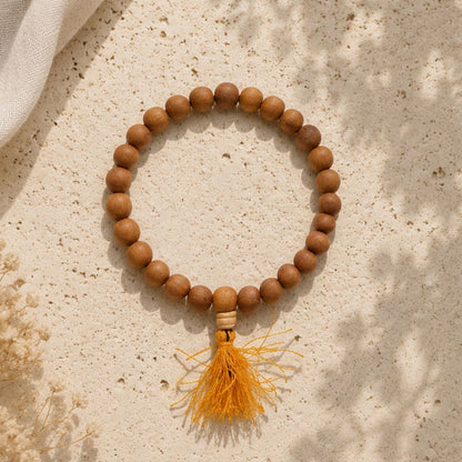 Wooden beaded bracelet with a yellow tassel on a textured beige surface