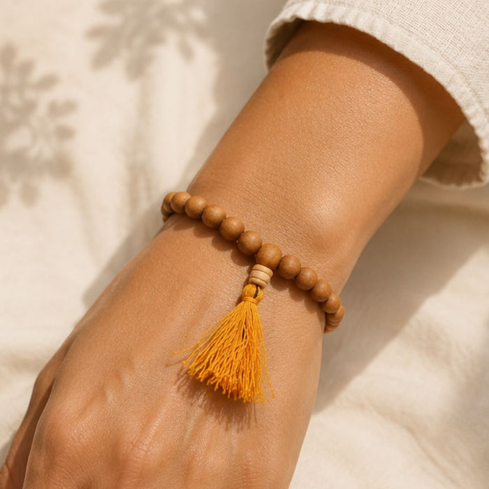 Wooden beaded bracelet with a yellow tassel on a wrist against a neutral background