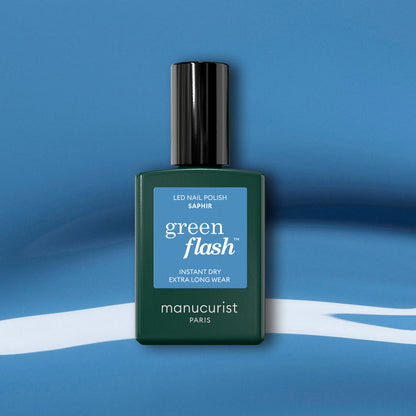 A Manucurist Saphir gel polish bottle with a black cap is displayed on a blue and white abstract background.