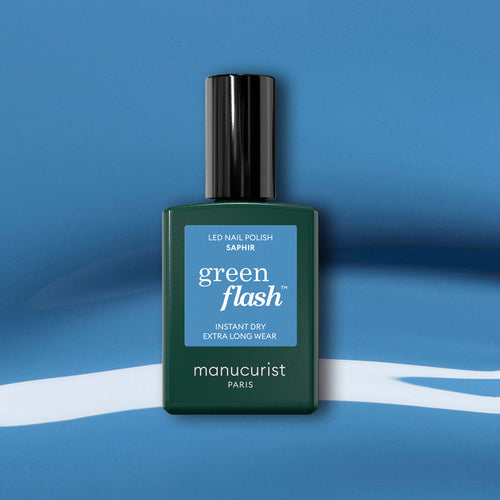 A Manucurist Saphir gel polish bottle with a black cap is displayed on a blue and white abstract background.