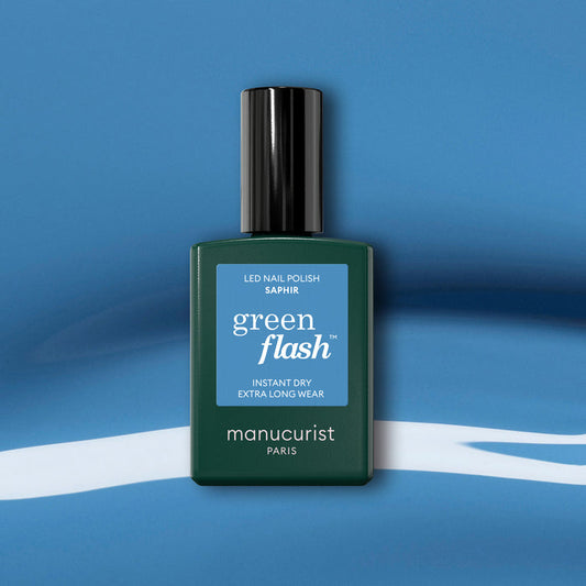 A Manucurist Saphir gel polish bottle with a black cap is displayed on a blue and white abstract background.